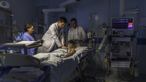 doctors in a hospital room doing chest compressions on a patient.