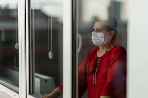 an older woman with a mask on looking through a window.
