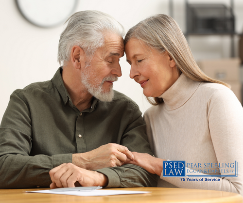 An older couple sits at a table, leaning close and holding hands while looking at each other with warm, affectionate expressions.